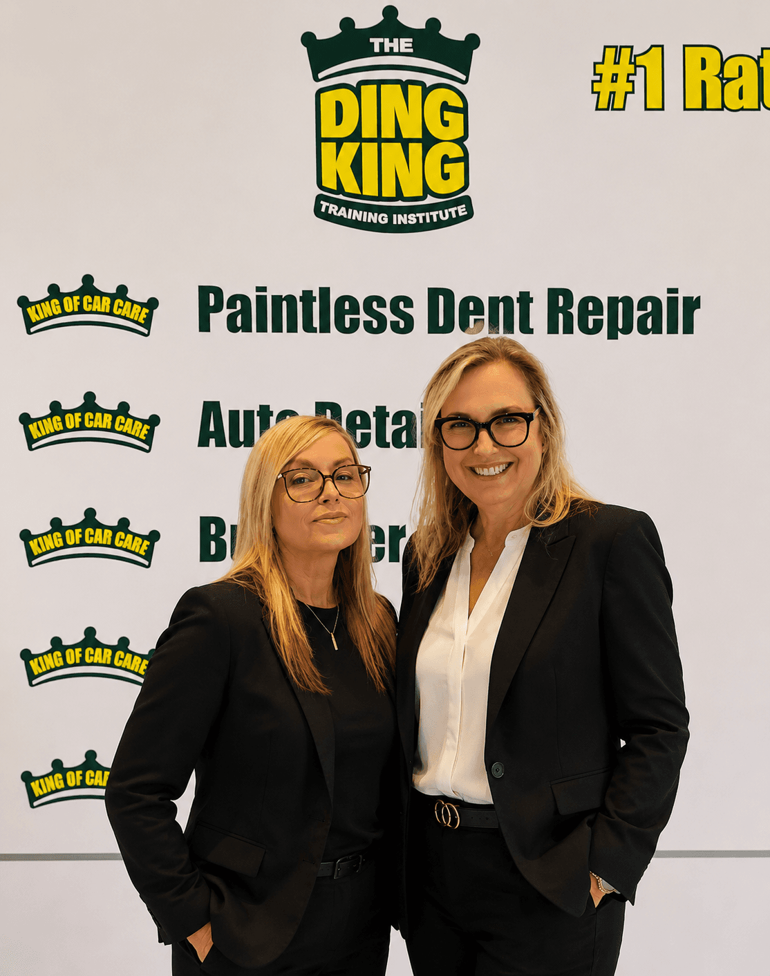 Two members of the school admissions team in front of a Ding King Training Institute backdrop listing paintless dent repair and auto detailing programs